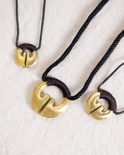 An Ifugao Lingling-o necklaces featuring a traditional brass Lingling-o pendant in varying sizes, shaped like a stylized open hoop with a central cut. The pendants are attached to dark braided or corded strings. Ifugao Lingling-O Necklace Jewelry | Narra Studio