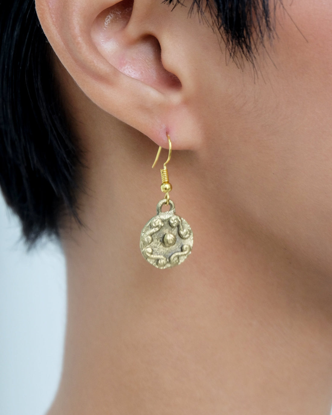 Tboli Hand-Cast Brass - Circle Earrings Womens Earrings.
A hand-cast brass earring crafted by the Tboli. The circular earring features traditional embossed swirl and dot patterns, hanging from a gold-tone hook.