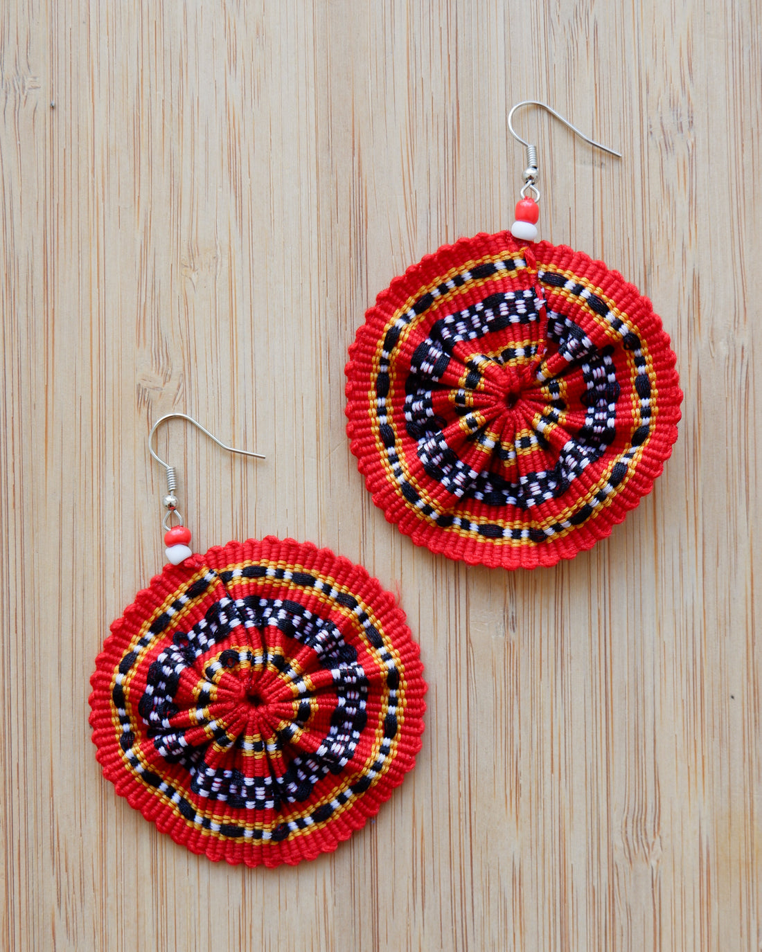 Pair of handwoven circular earrings with vibrant red, black, yellow, and white geometric patterns, inspired by traditional Kalinga textiles. Each earring features gathered woven fabric and a red-and-white beaded hook.