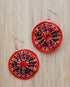 Pair of handwoven circular earrings with vibrant red, black, yellow, and white geometric patterns, inspired by traditional Kalinga textiles. Each earring features gathered woven fabric and a red-and-white beaded hook.
