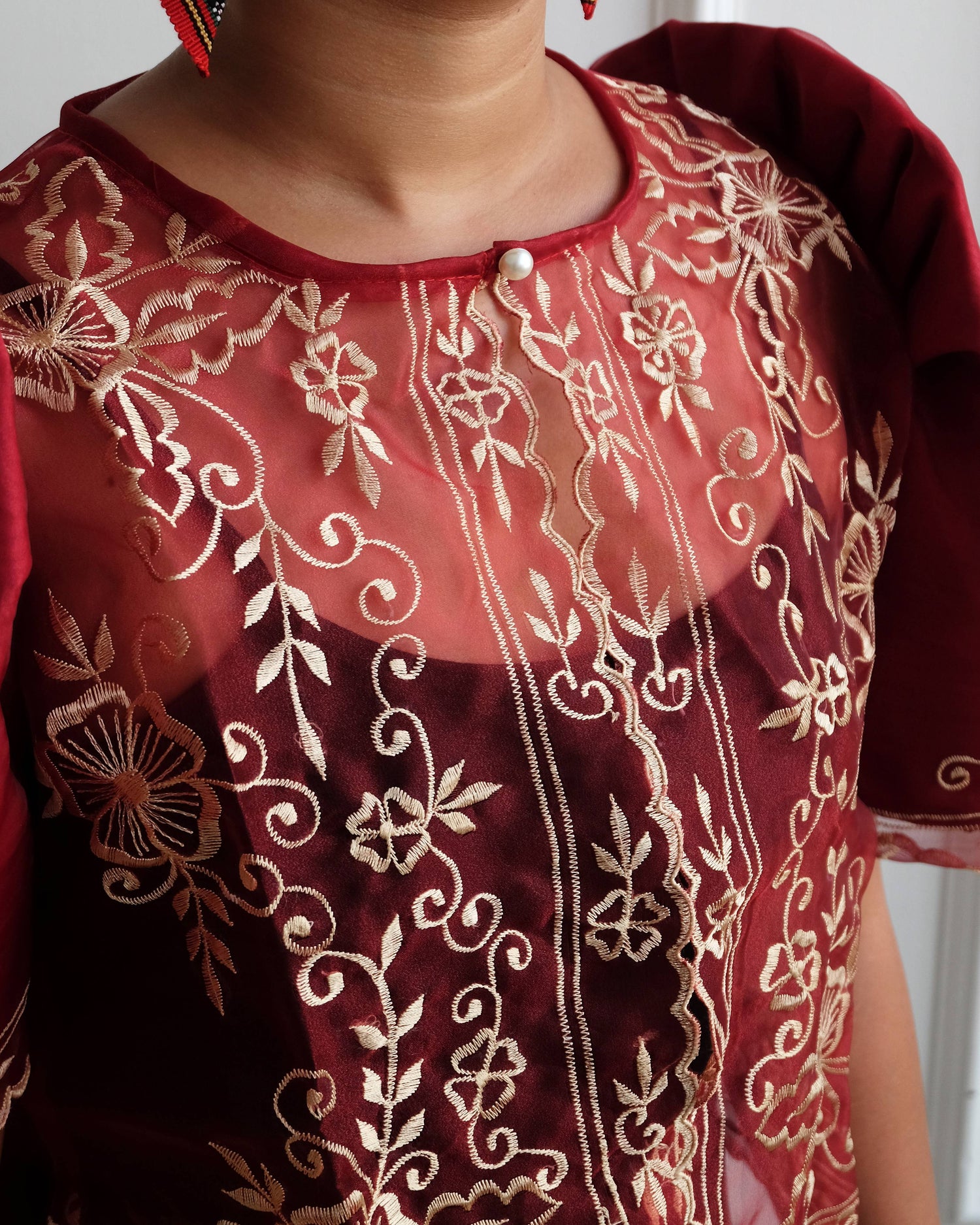 A maroon Filipiniana bolero blouse with floral embroidery on sheer organza fabric, featuring iconic butterfly sleeves.