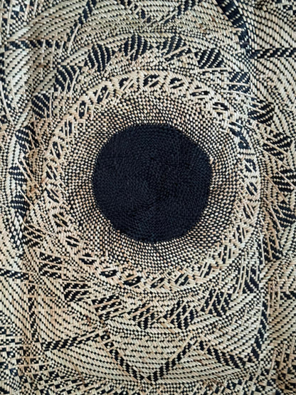 Black Banig Mat. A round black woven banig mat with bold geometric patterns—triangles, diamonds, and lines radiate from a solid center.