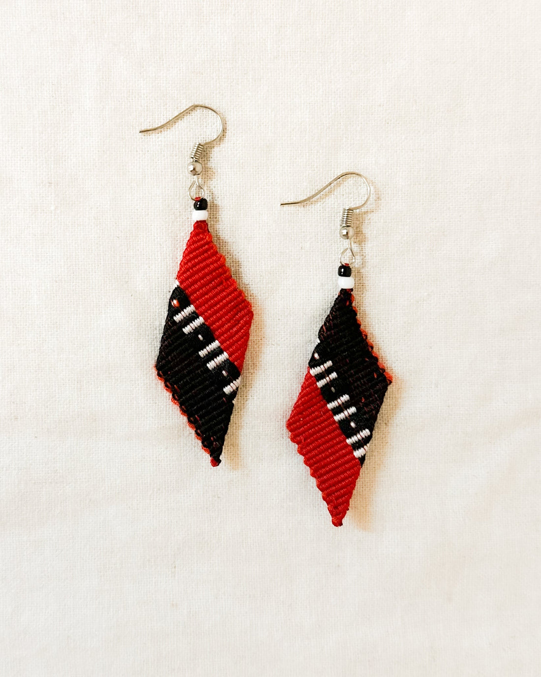 A pair of handwoven Kalinga earrings in a red and black trapezium design, featuring white and black bead accents, blending traditional Filipino craftsmanship with modern, artisan-made style.