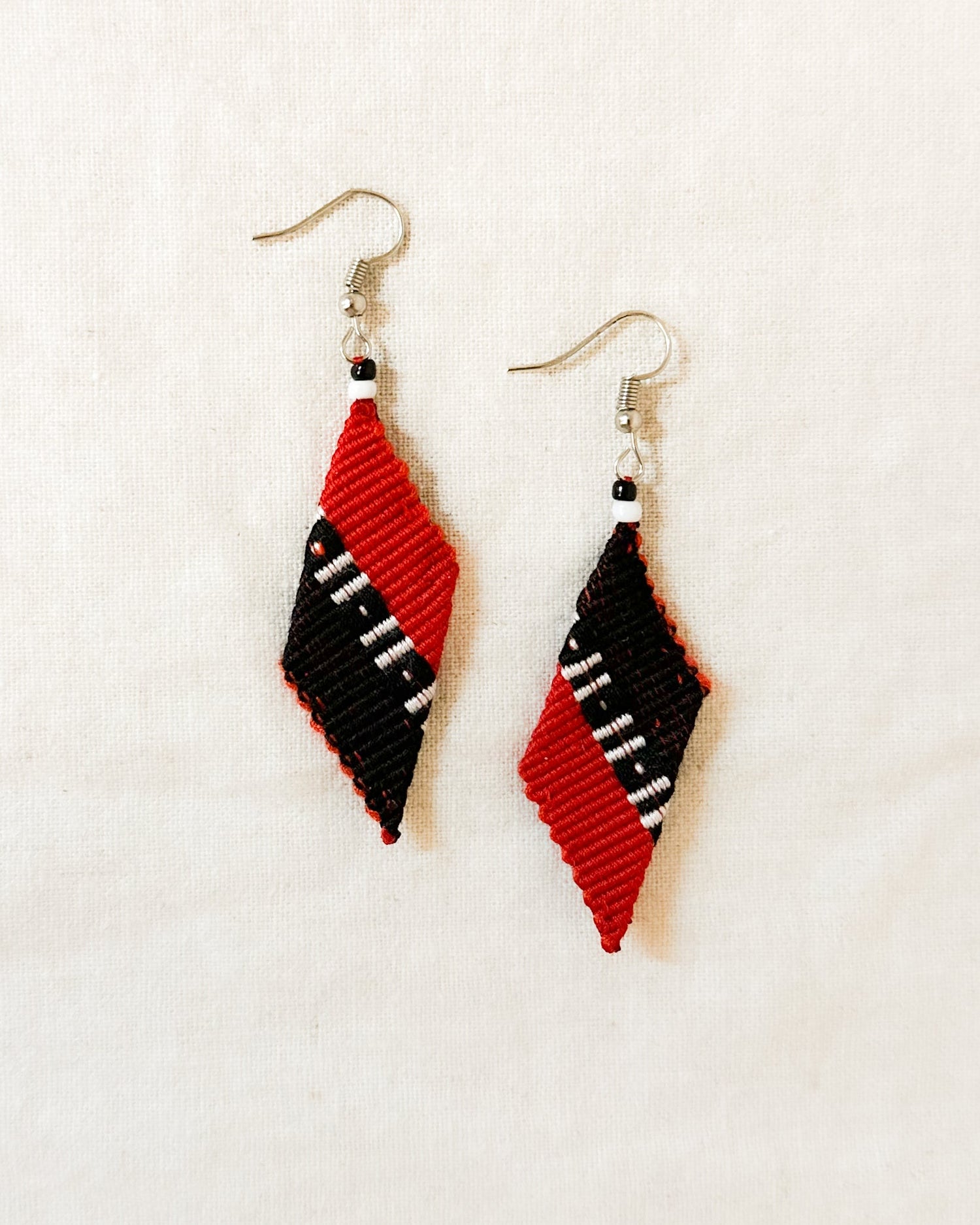A pair of handwoven Kalinga earrings in a red and black trapezium design, featuring white and black bead accents, blending traditional Filipino craftsmanship with modern, artisan-made style.