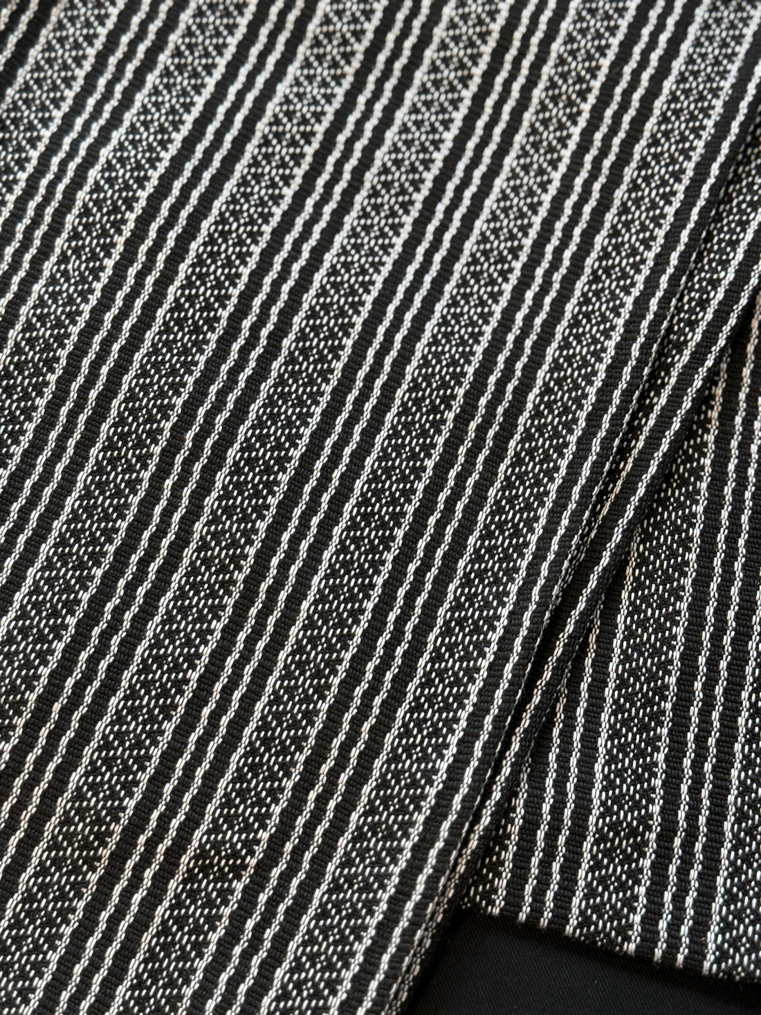 Handwoven sablay sash featuring horizontal patterns in black and white. The intricate geometric designs include X and diamond motifs, arranged in alternating bands that reflect traditional Filipino textile artistry.