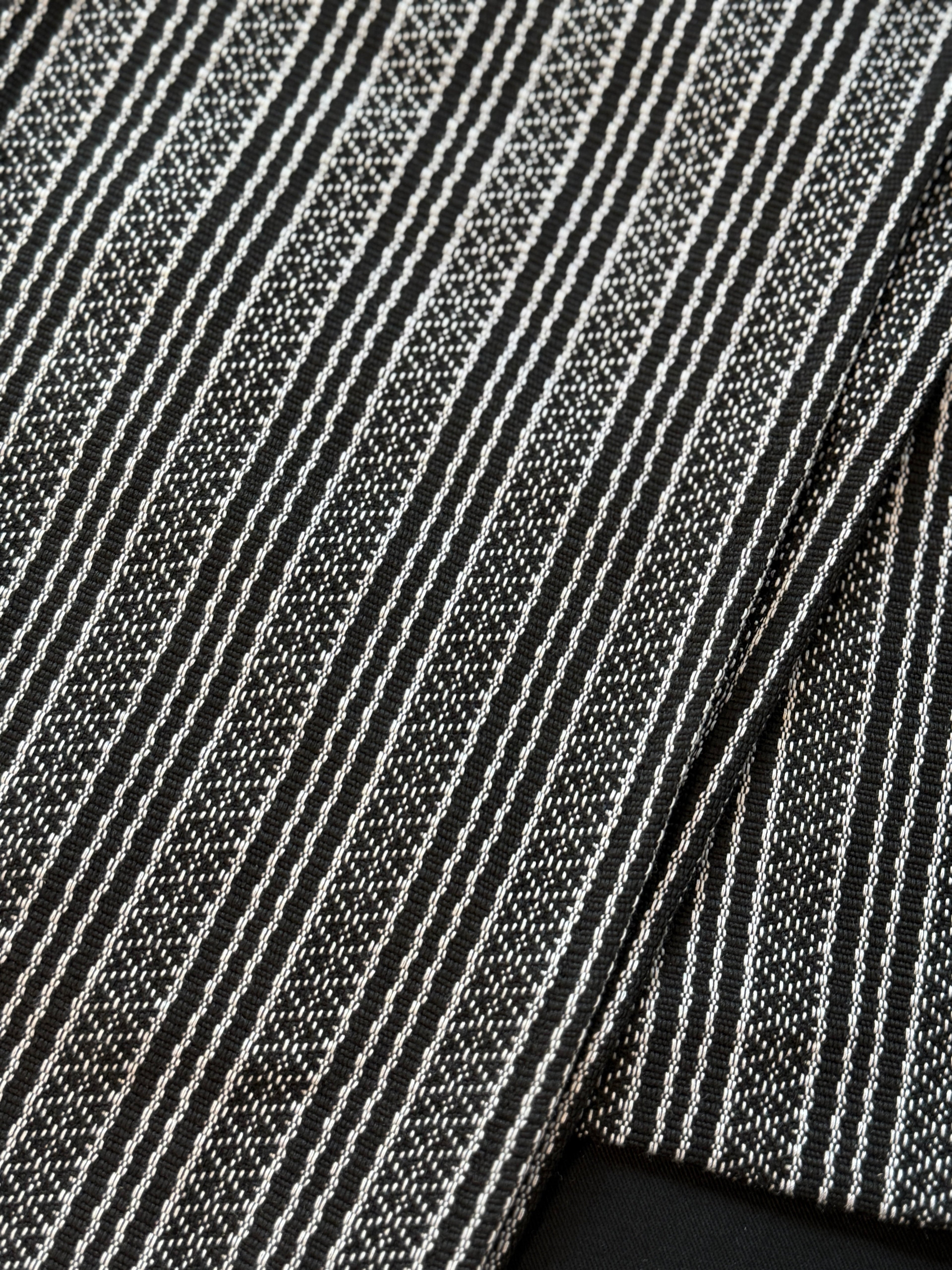 Handwoven sablay sash featuring horizontal patterns in black and white. The intricate geometric designs include X and diamond motifs, arranged in alternating bands that reflect traditional Filipino textile artistry.