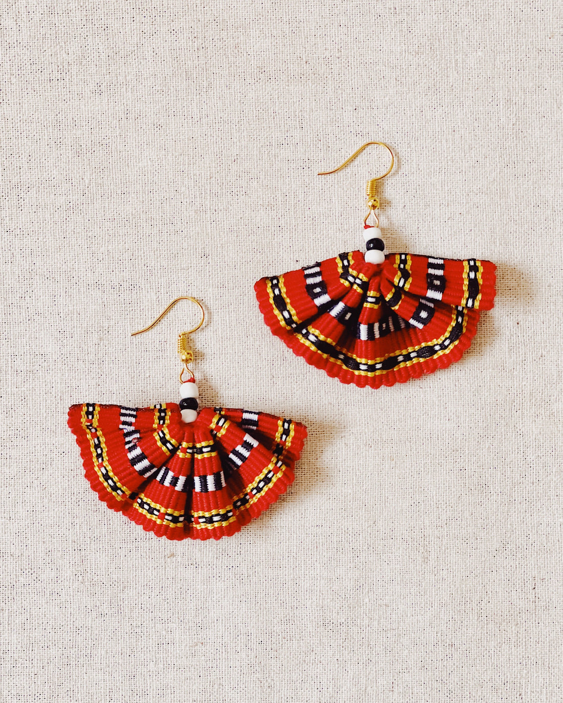 A pair of handwoven Kalinga fan earrings featuring a semi-circular, pleated design in vibrant red fabric with black, white, and yellow tones.